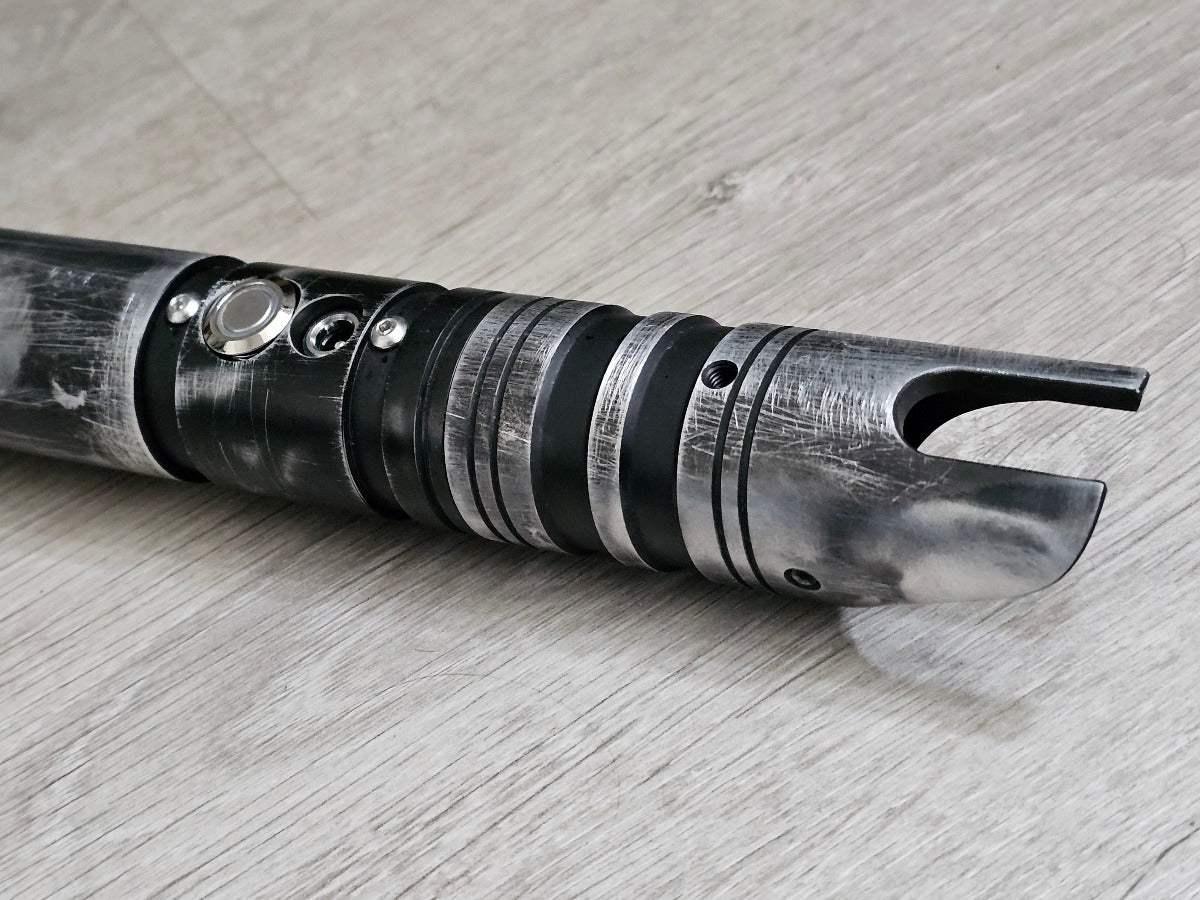 Weathered Ezra Bridger lightsaber hilt replica with black and silver detailing on wood floor