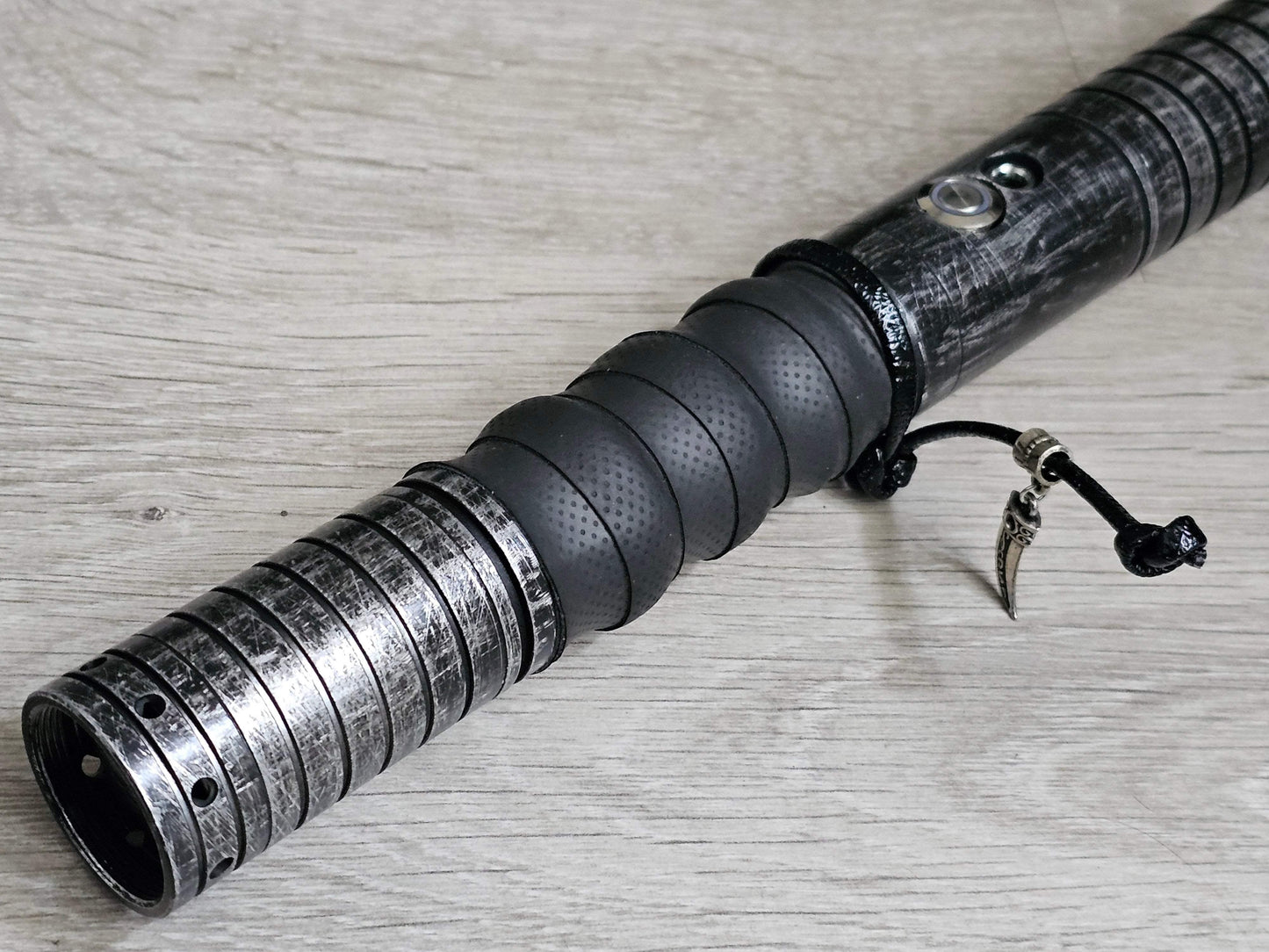 Custom lightsaber hilt inspired by Cal Kestis from Star Wars, featuring a weathered metal design, black grip, and unique charm.